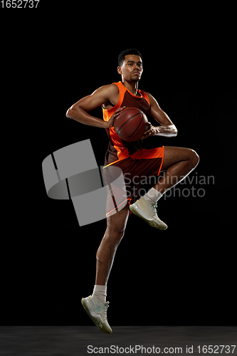 Image of Young african basketball player training on black studio background.