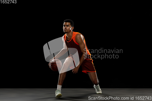 Image of Young african basketball player training on black studio background.