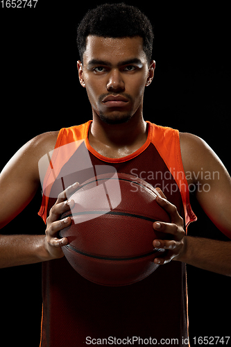 Image of Young african basketball player training on black studio background.