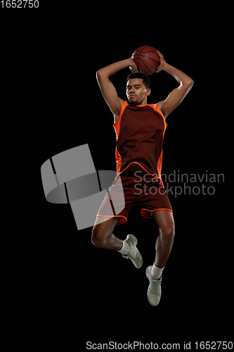 Image of Young african basketball player training on black studio background.