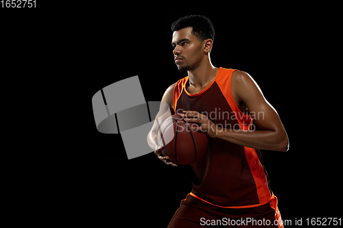 Image of Young african basketball player training on black studio background.