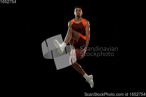 Image of Young african basketball player training on black studio background.