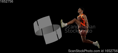 Image of Young african basketball player training on black studio background.