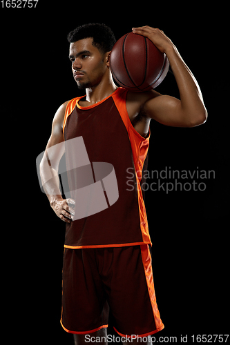 Image of Young african basketball player training on black studio background.