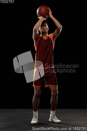 Image of Young african basketball player training on black studio background.