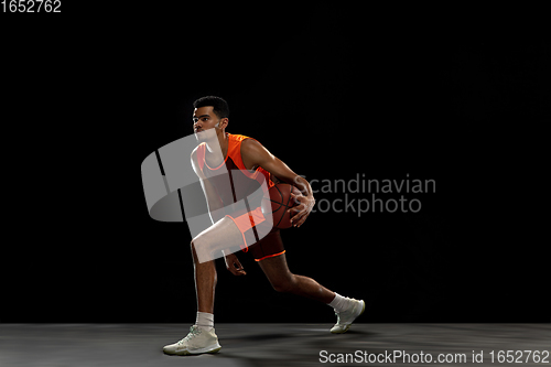 Image of Young african basketball player training on black studio background.