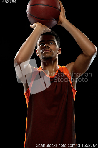 Image of Young african basketball player training on black studio background.