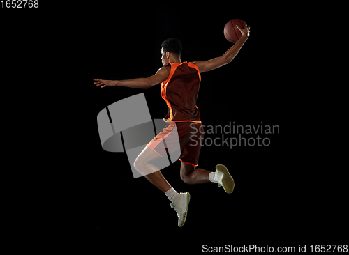 Image of Young african basketball player training on black studio background.