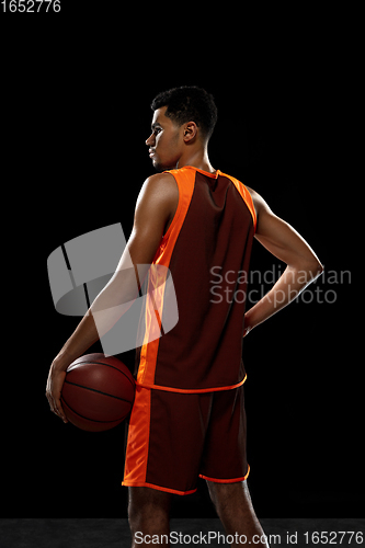 Image of Young african basketball player training on black studio background.