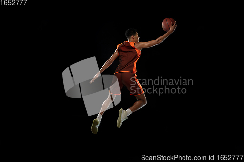 Image of Young african basketball player training on black studio background.