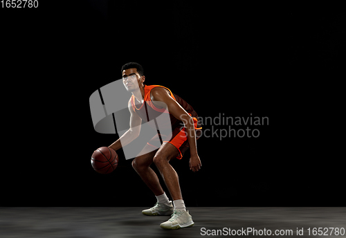 Image of Young african basketball player training on black studio background.