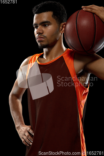 Image of Young african basketball player training on black studio background.