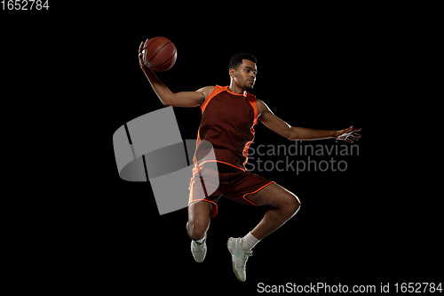 Image of Young african basketball player training on black studio background.