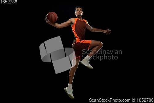 Image of Young african basketball player training on black studio background.