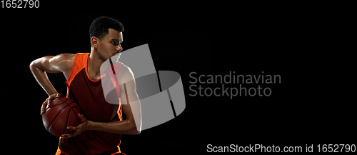 Image of Young african basketball player training on black studio background.