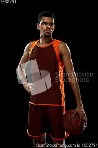 Image of Young african basketball player training on black studio background.