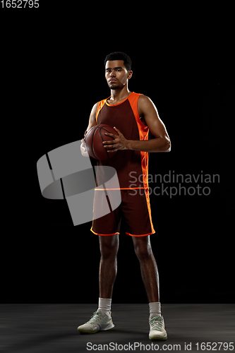 Image of Young african basketball player training on black studio background.