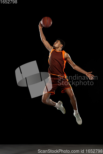 Image of Young african basketball player training on black studio background.