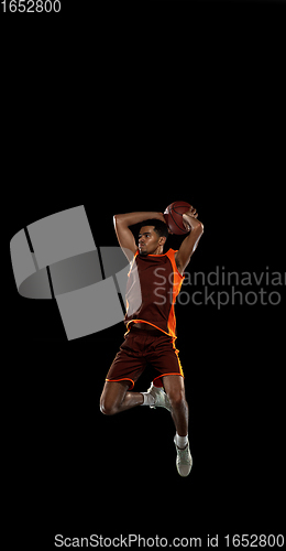 Image of Young african basketball player training on black studio background.