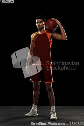 Image of Young african basketball player training on black studio background.