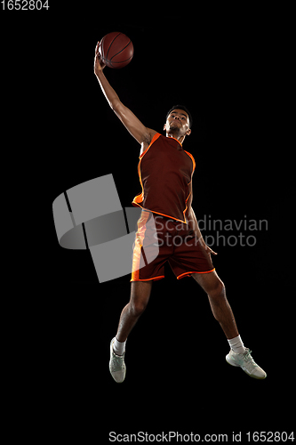 Image of Young african basketball player training on black studio background.