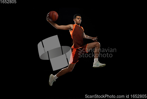 Image of Young african basketball player training on black studio background.