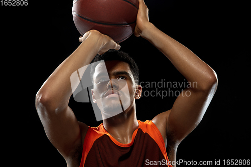 Image of Young african basketball player training on black studio background.