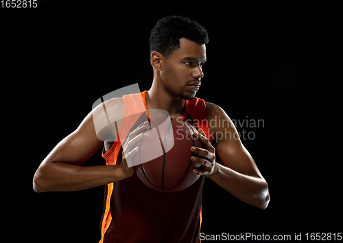 Image of Young african basketball player training on black studio background.