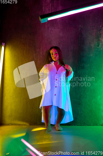 Image of Caucasian female inclusive model posing on studio background in neon light
