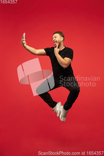 Image of Full length portrait of young successfull high jumping man gesturing isolated on red studio background