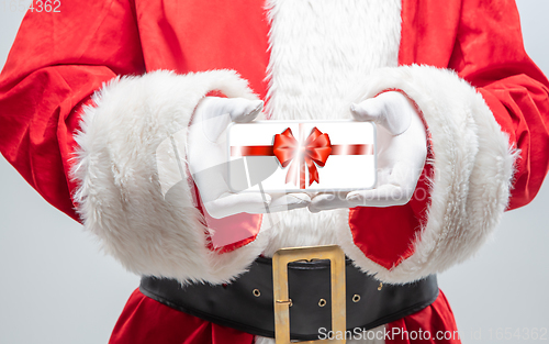 Image of Close up hands of Santa Claus holding device with gift decoration on the screen