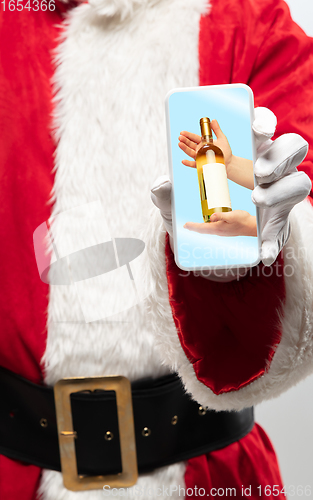 Image of Close up hands of Santa Claus holding device with hands giving wine on the screen