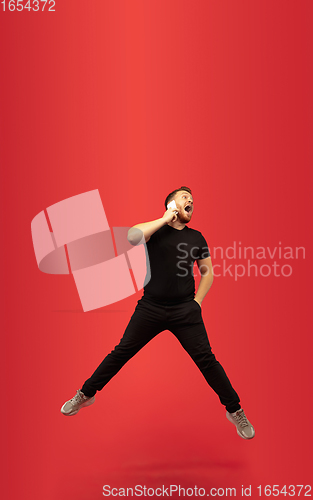 Image of Full length portrait of young successfull high jumping man gesturing isolated on red studio background