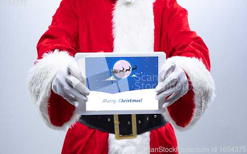 Image of Close up hands of Santa Claus holding device with postcard decoration on the screen