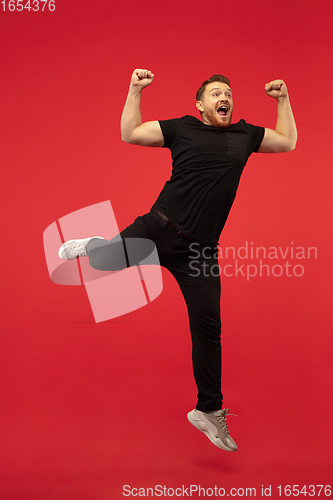 Image of Full length portrait of young successfull high jumping man gesturing isolated on red studio background