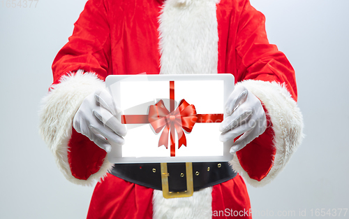 Image of Close up hands of Santa Claus holding device with gift decoration on the screen