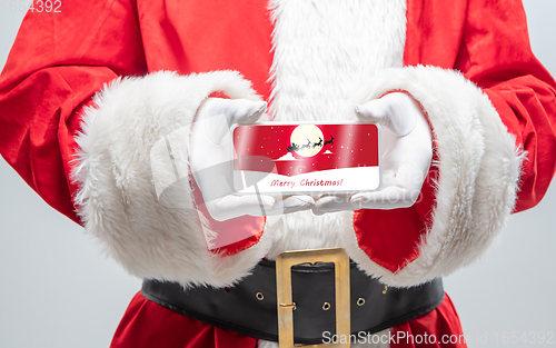 Image of Close up hands of Santa Claus holding device with postcard decoration on the screen