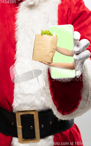 Image of Close up hands of Santa Claus holding device with hands giving food on the screen