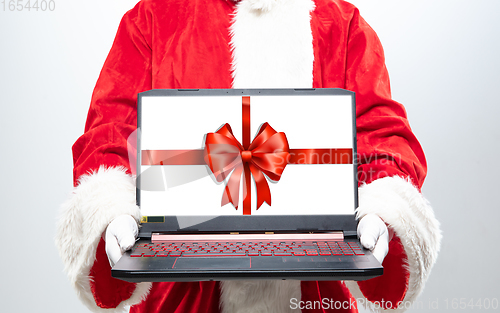 Image of Close up hands of Santa Claus holding device with gift decoration on the screen