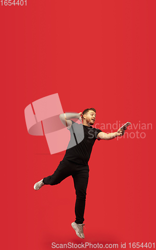 Image of Full length portrait of young successfull high jumping man gesturing isolated on red studio background