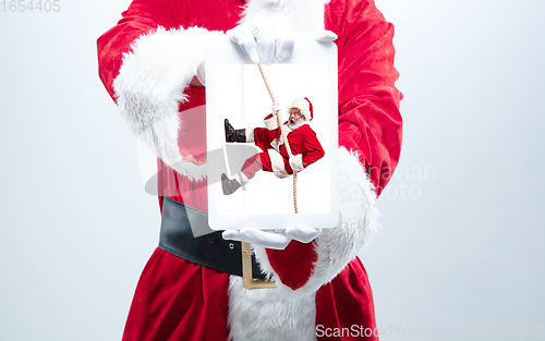 Image of Close up hands of Santa Claus holding device with another climbing Santa on the screen