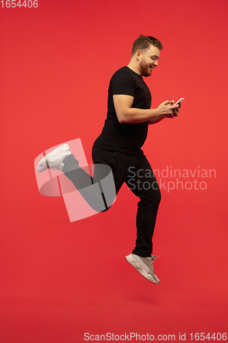 Image of Full length portrait of young successfull high jumping man gesturing isolated on red studio background