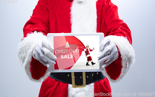 Image of Close up hands of Santa Claus holding device with another climbing Santa on the screen