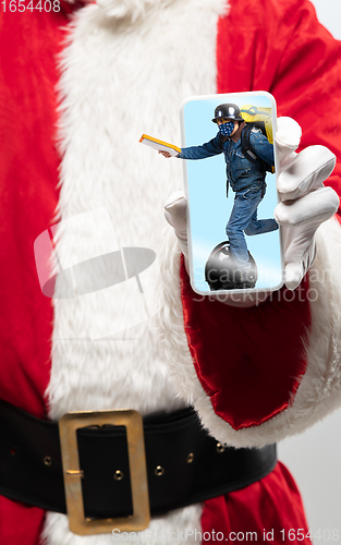 Image of Close up hands of Santa Claus holding device with riding deliveryman on the screen