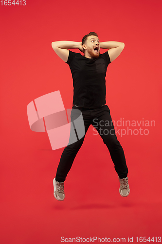 Image of Full length portrait of young successfull high jumping man gesturing isolated on red studio background