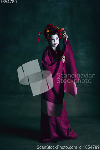 Image of Young japanese woman as geisha on dark green background. Retro style, comparison of eras concept.