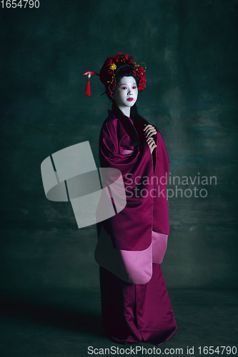 Image of Young japanese woman as geisha on dark green background. Retro style, comparison of eras concept.