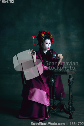 Image of Young japanese woman as geisha on dark green background. Retro style, comparison of eras concept.