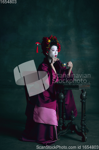 Image of Young japanese woman as geisha on dark green background. Retro style, comparison of eras concept.