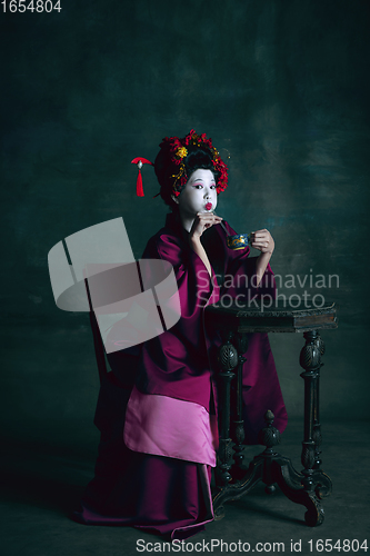 Image of Young japanese woman as geisha on dark green background. Retro style, comparison of eras concept.